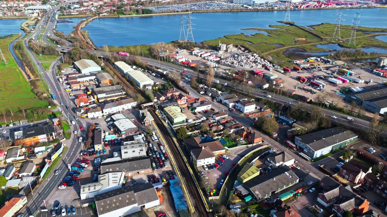 冬のイギリス、サウサンプトンにある川の西側、トットン郊外上空からの空撮パニングショット。交通量の多い道路を車が走り、ボートが浮かぶ青い川の水面には太陽の光が反射している。