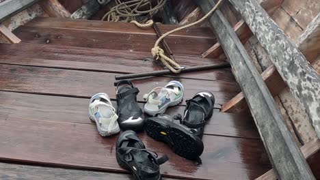 a collection of sandals and shoes neatly placed on a wooden boat deck with visible ropes.