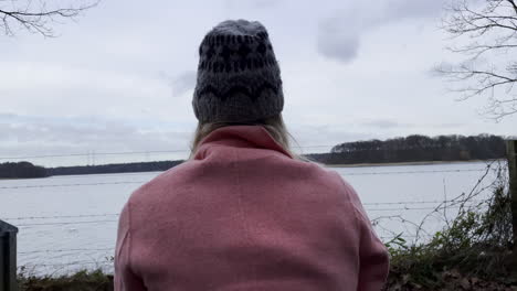 fashionable blond woman with pink coat and beanie enjoying beautiful view of natural lake and nature landscape