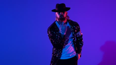 man in sequined jacket and hat posing against a vibrant blue and purple background