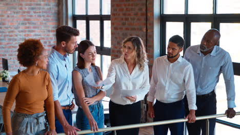 businesswoman leading team meeting in busy multi-cultural office handing out documents