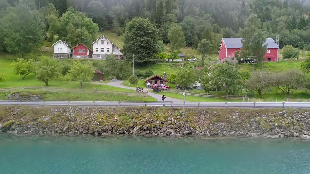 Ripresa aerea con movimento dolly inverso di una bellissima donna bruna in piedi accanto al fiordo di Oppstrynsvatnet e alla strada, che rivela l'ambiente circostante, Stryn.