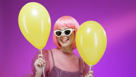 portrait shot of beautiful woman wearing a pink wig and glasses and dancing with yellow balloons