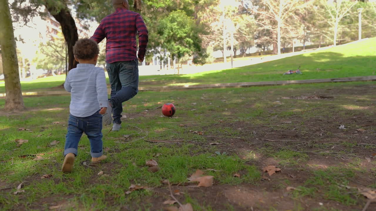 padre afroamericano jugando al fútbol con un pequeño hijo de raza mixta