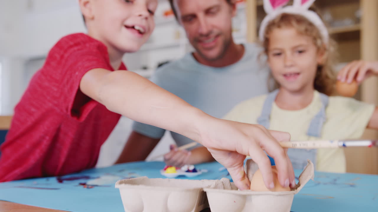padre con niños con orejas de conejo decorando huevos de pascua en casa juntos