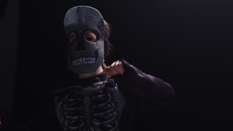 studio shot of child dressed up in skeleton costume trick or treating at halloween dancing against black background 2