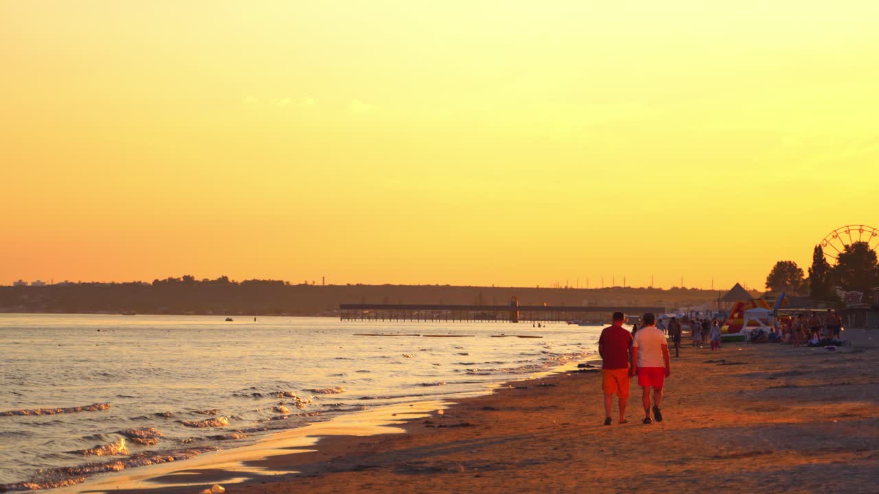 Back view of two men are walking on the beach at sunset. People walking in the evening on the beautiful sea background outdoors.