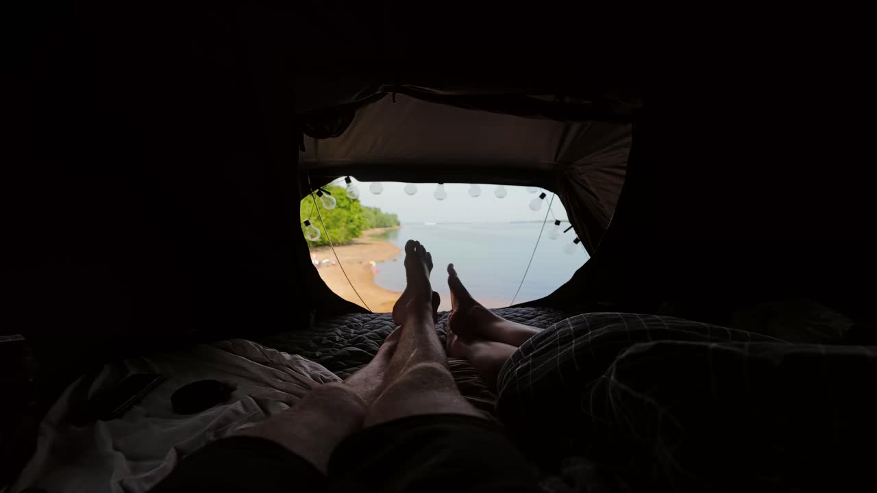 Peaceful morning light fills camper tent as couple rests beside calm reservoir