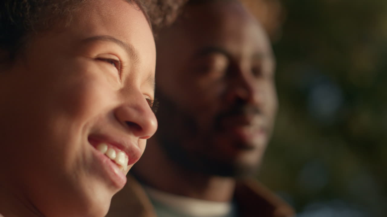 Portrait d'une petite fille souriante aux côtés de son père, profitant du soleil doré du soir.