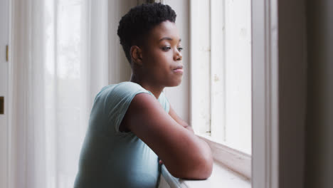 mujer afroamericana mirando por la ventana en casa