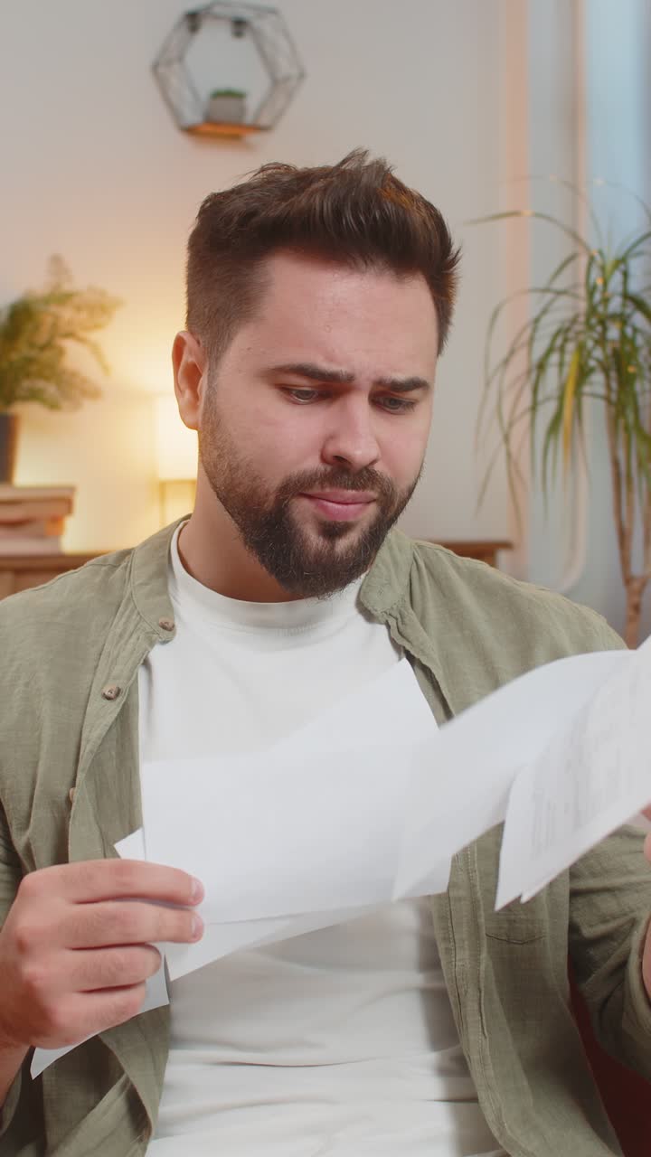 joven caucásico estresado sentado en el sofá revisando facturas de deuda no pagadas y vomitando en el aire