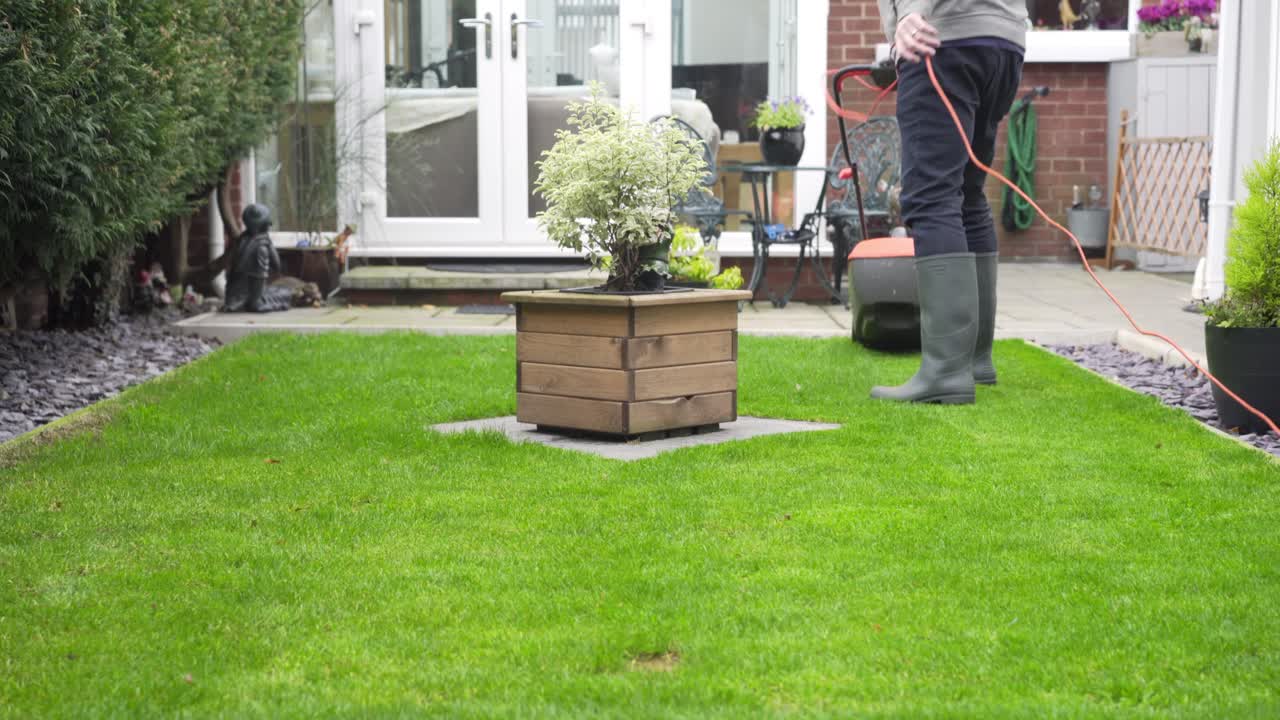 Man with green boots on cutting green grass with mower in garden, autumn time