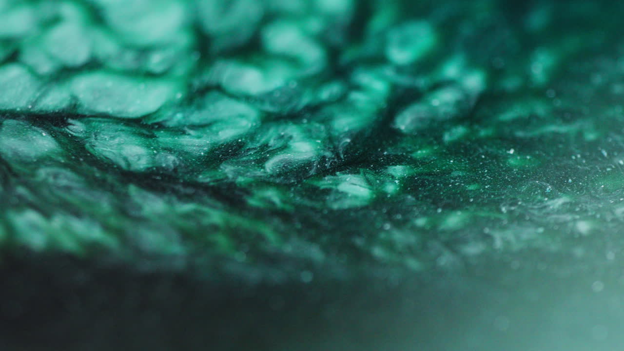 Macro shot of green, cyan, dark green, grey, and blue ink flowing in fluid abstract motion, resembling a river