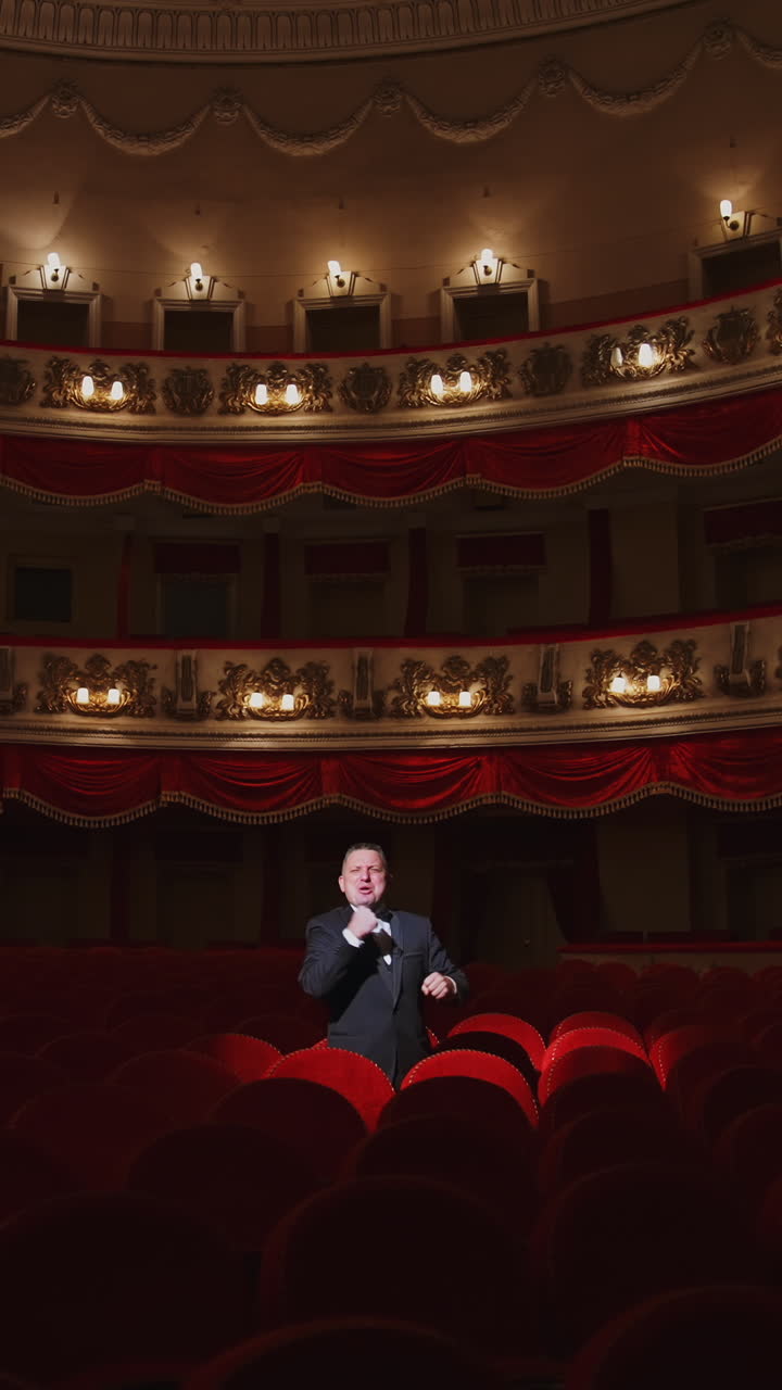Actor among red seats in empty concert hall. Man in suit standing in beautiful large empty auditorium and talking something. Lockdown in the world. Vertical video