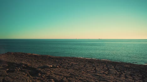 ocean shoreline cliff rocks, cargo boats away at sunset with blue sky wide angle 4k