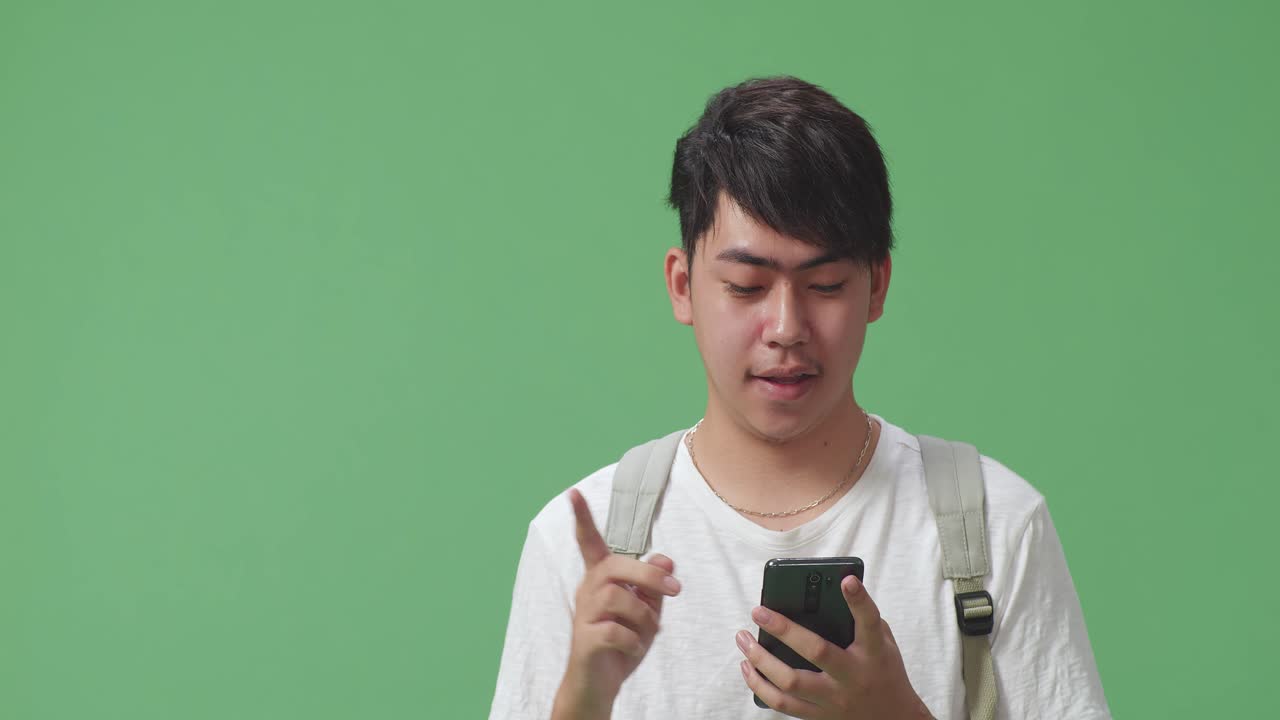 녹색 스크린 스튜디오에서 휴대전화와 직접 손가락을 사용하는 아시아 남성 학생의 클로즈업