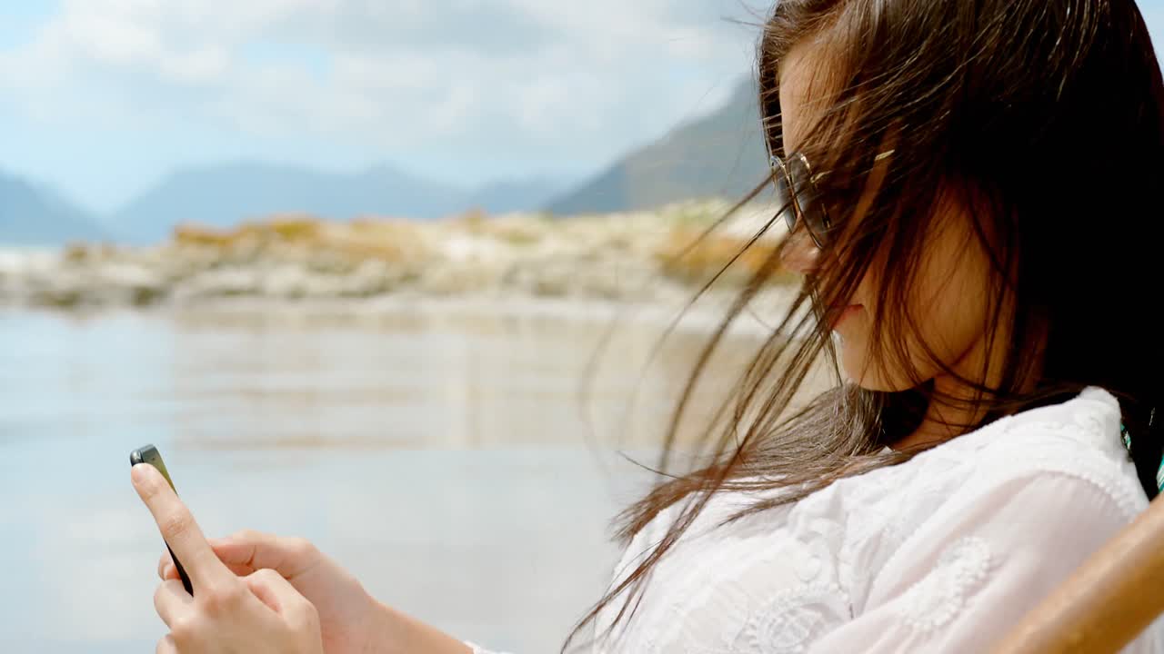 vista lateral de una joven mujer caucásica usando teléfono móvil en la playa 4k