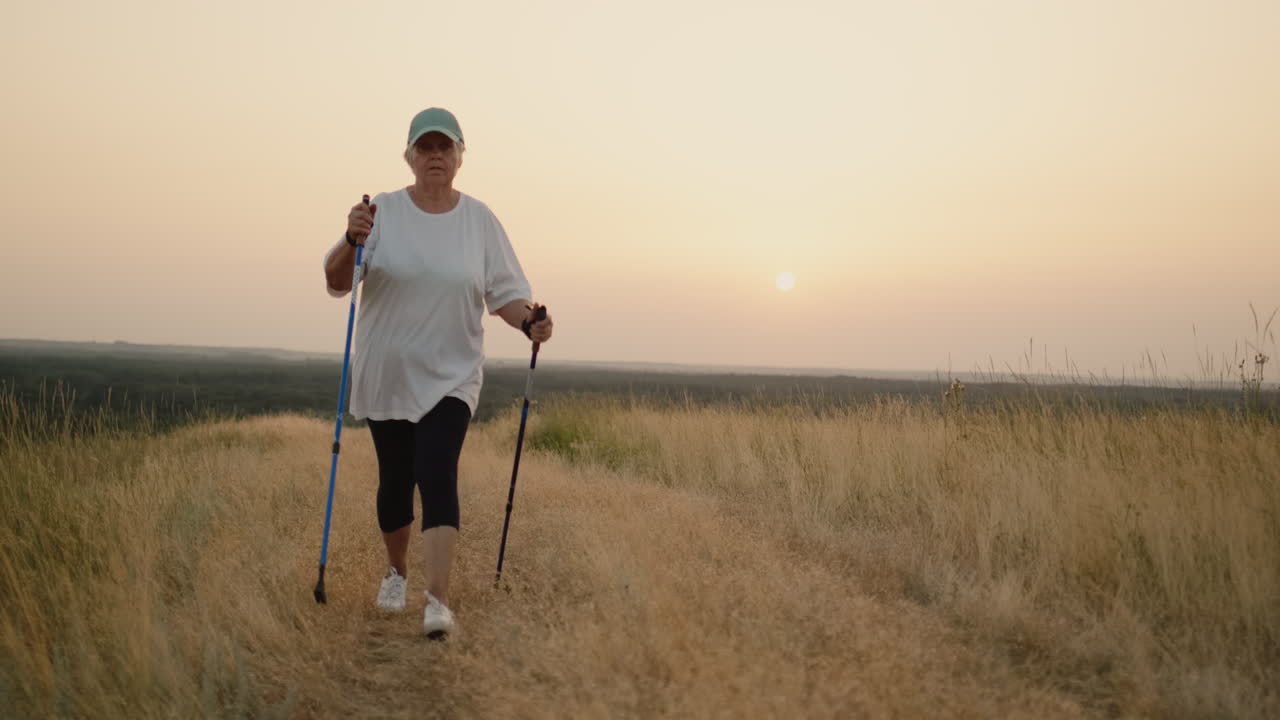 En eldre kvinne med nordiske gåstaver går fremover gjennom et naturskjønt sted 2