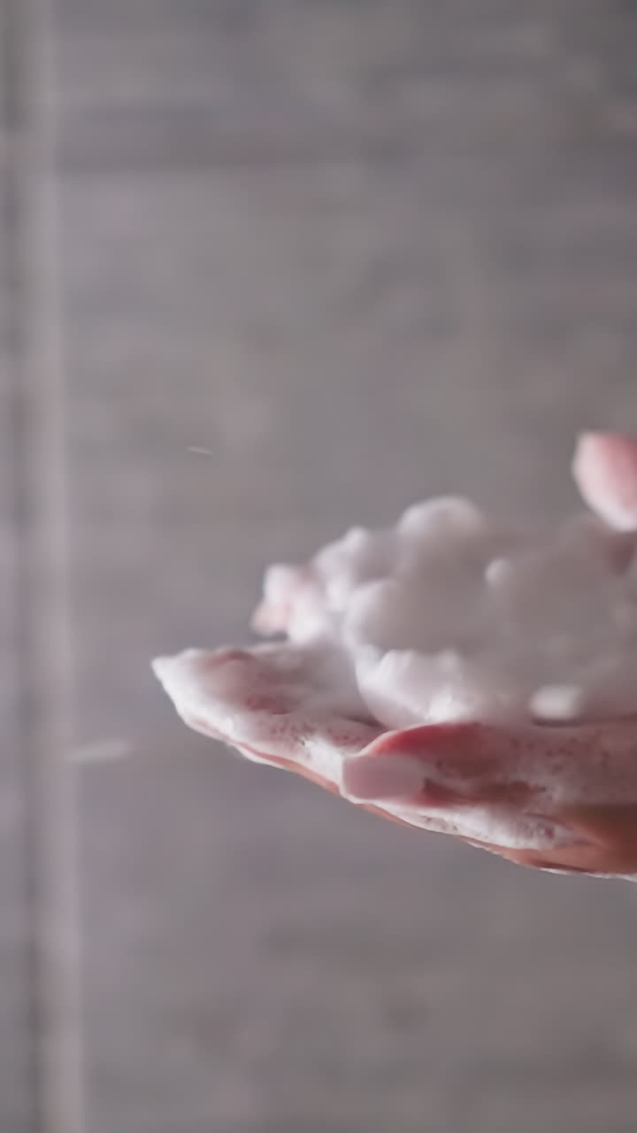 여성은 샤워 유에서 손에서 거품을 불어내고, 여성은 집 화장실에서 목욕하는 동안 비누 거품으로 재미를 느니다.