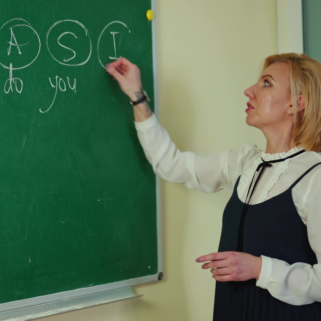 Teacher writes on blackboard. Female pedagogue writing on a green chalkboard and telling the rules to students in the classroom. Education concept.