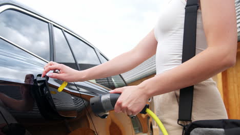 woman plugging a charger in an electric car and entering a house door, close up