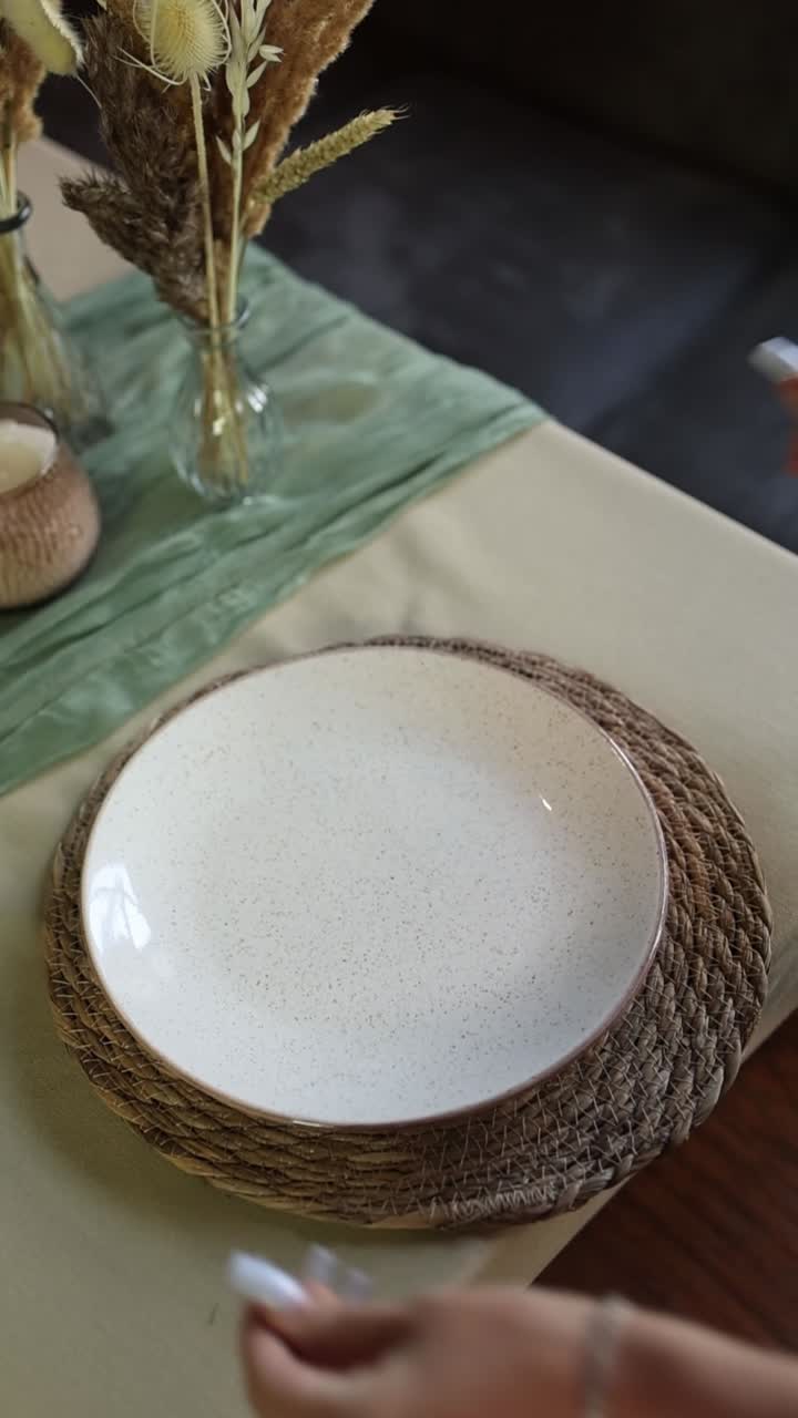 Mani che posizionano un piatto di ceramica su una tovaglietta intrecciata per un'apparecchiatura rustica.