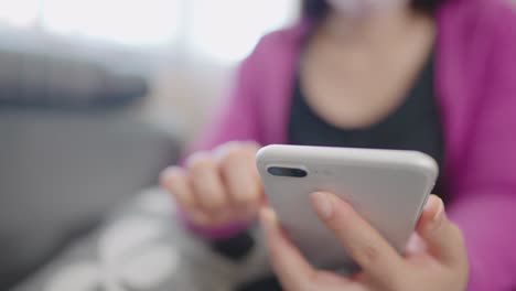 una mujer en primer plano sentada en un sofá sosteniendo un teléfono inteligente para comprar en línea en casa