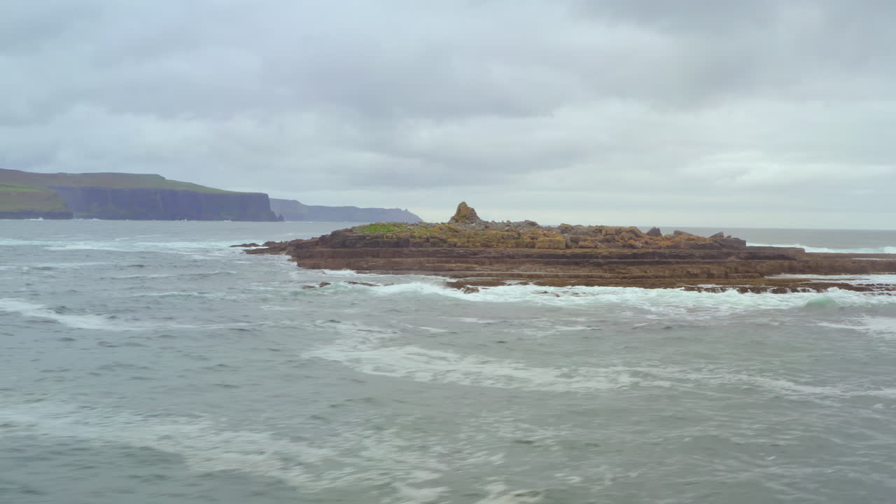 Dynamic low-angle aerial orbit around Crab Island, with Cliffs of Moher in the background. Wide establishing shot