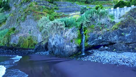 pequeña cascada que fluye hacia las rocas y la playa de arena negra en seixal, isla de madeira, portugal