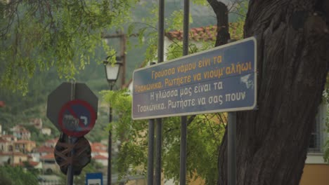 Cartel-Que-Presenta-La-Clásica-Ciudad-De-Leonidio,-Grecia,-En-La-Entrada-Debajo-Del-Viejo-árbol