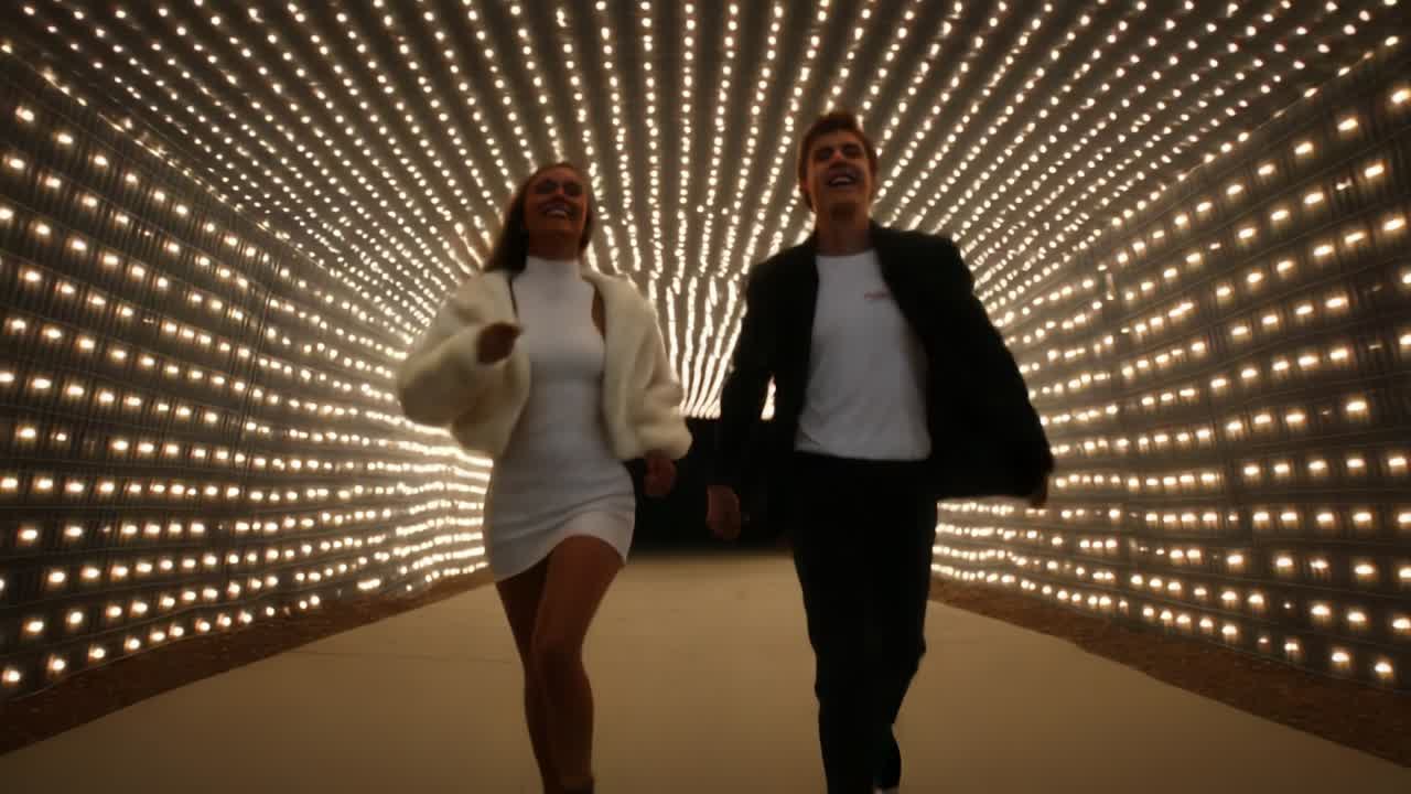 Joyful Journey Through a Wall of Light: A Young Couple Runs Together in a Dynamic and Vibrant Setting, Captured in Two Frames from a Video Full of Energy and Emotion, Emphasizing their Connection and Excitement