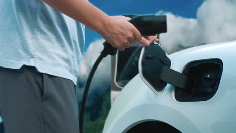 progressive man charging electric car and traveling through nature and mountains