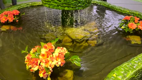 Fuente-De-Agua-Con-Flores-Y-Plantas,-Tiro-Inclinado