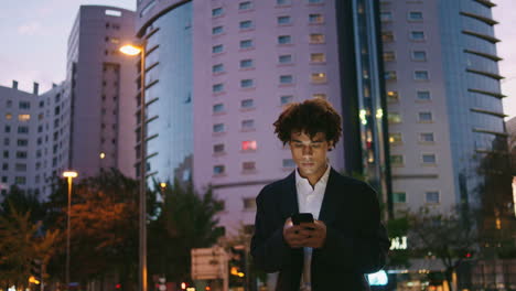 Serious-manager-working-phone-at-dusk-street.-Young-business-man-typing-mobile