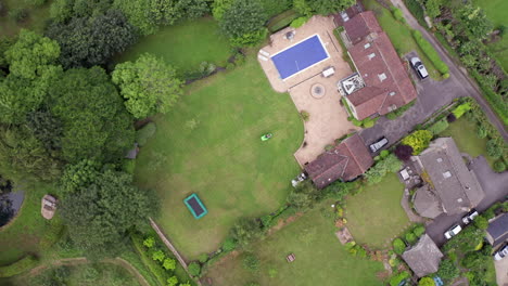 Falling-Aerial-Shot-of-Man-Mowing-Lawn-of-Home-on-Summer’s-Day-using-Ride-On-Lawnmower-from-Birds-Eye-View-Perspective