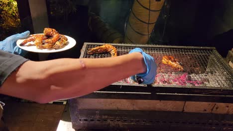 local chef taking grilled shrimp of hot plate, close up view