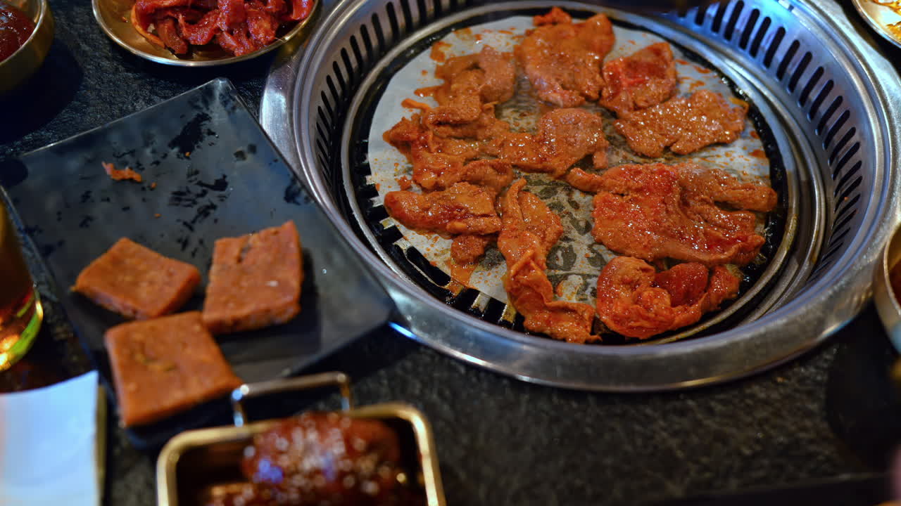 Man putting French fries on a table near multiple pieces of meat cooking at a restaurant in Copenhagen, Denmark