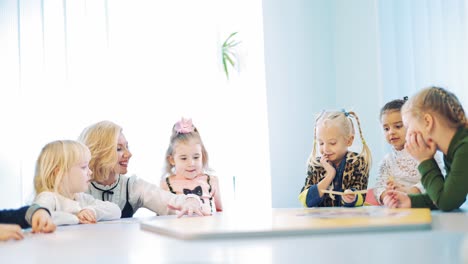 children with their teacher together at round table in class. little kids studying english while playing with pictures at elementary school.