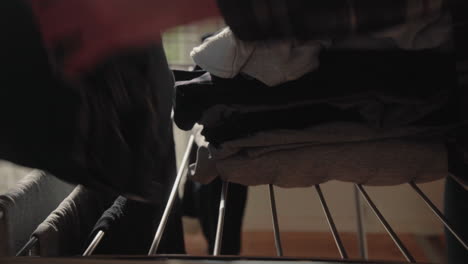 young male collecting and folding dry clean clothes from dryer at home in sunlit modern living room collecting a pile from the rack 4k