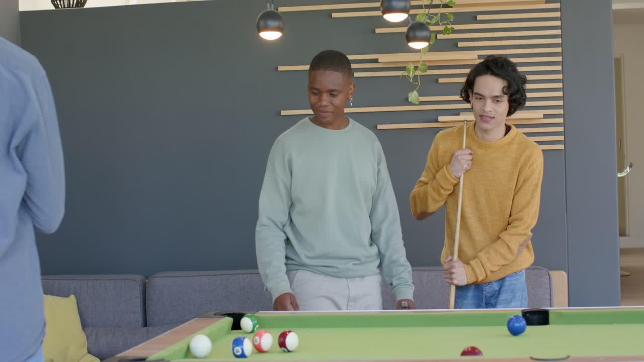 Diverse male friends stepping to pool table in lounge lining shot and scattering balls for points