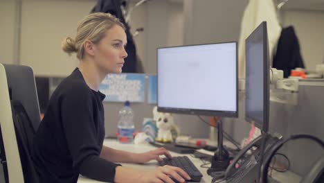 a blonde female employee is working on a computer with two screens
