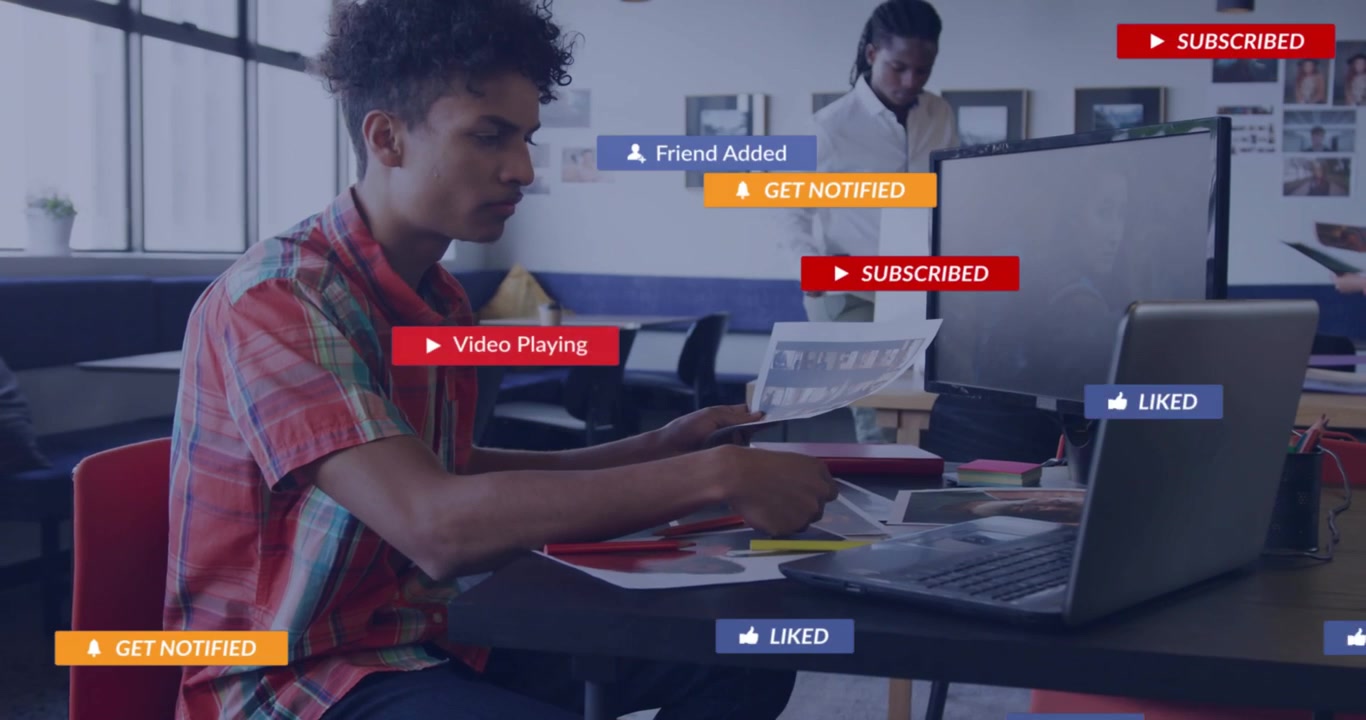 Seated man tapping laptop in office, creating social media badges around desk showing engagement