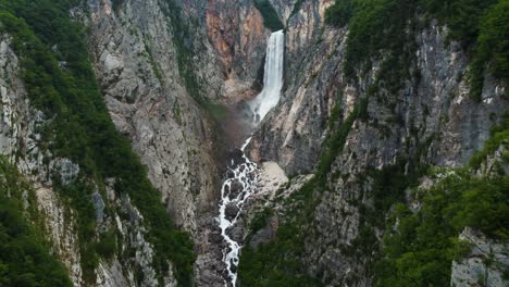 Vuelo-Hacia-Atrás-De-Un-Dron-Cinematográfico-Que-Muestra-La-Caída-De-La-Cascada-De-Boka-Entre-Acantilados-Cerca-Del-Nacional-De-Triglav,-Eslovenia