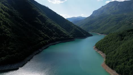flying over the turquiose lake pivsko near pluzine surrounded by green forrests and mountains in montenegro druing august summertime