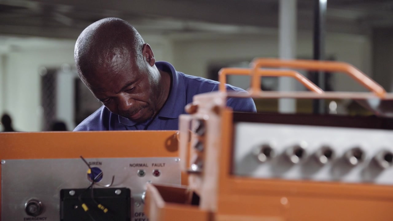 African Industrial Electrician working on some orange industrial equipment