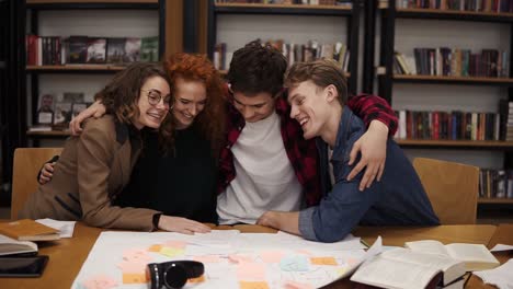 Retrato-De-Diversos-Amigos-Compañeros-De-Clase-Sentados-En-La-Mesa-En-La-Biblioteca-Universitaria-Abrazándose,-Abrazándose-Unos-A-Otros