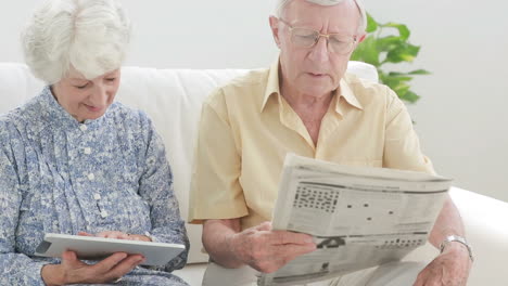 Old-couple-using-a-tablet-and-a-newspaper