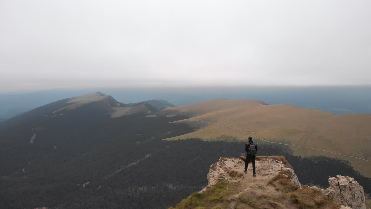 이탈리아 돌로미티 계곡이 내려다보이는 바위 가장자리로 걸어가는 젊은 모델을 지나는 드론의 공중 촬영