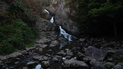 Aerial-drone-forward-ascending-over-rocks-of-stream-with-Mortain-big-waterfall,-Manche-in-France