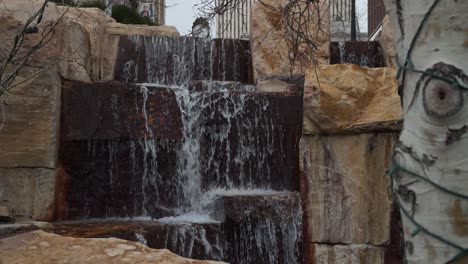 camera pans up from greenery to reveal cascading stone waterfall in public park